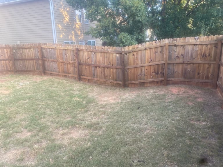 Wooden fence enclosure in residential backyard with sparse grass and trees in background