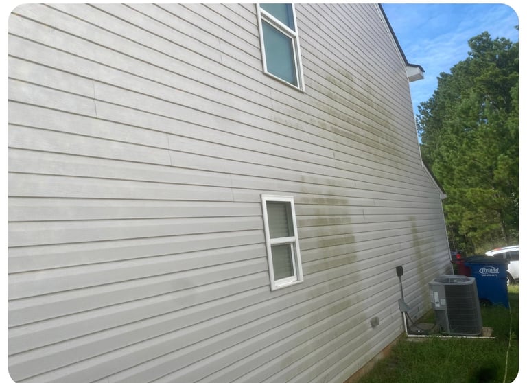 Gray horizontal siding on side of residential house with two windows and green trees visible in background