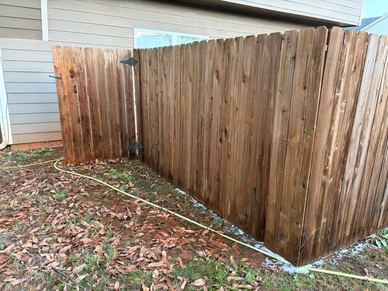 Wooden privacy fence enclosure in a residential backyard with mulch ground covering and house siding visible.