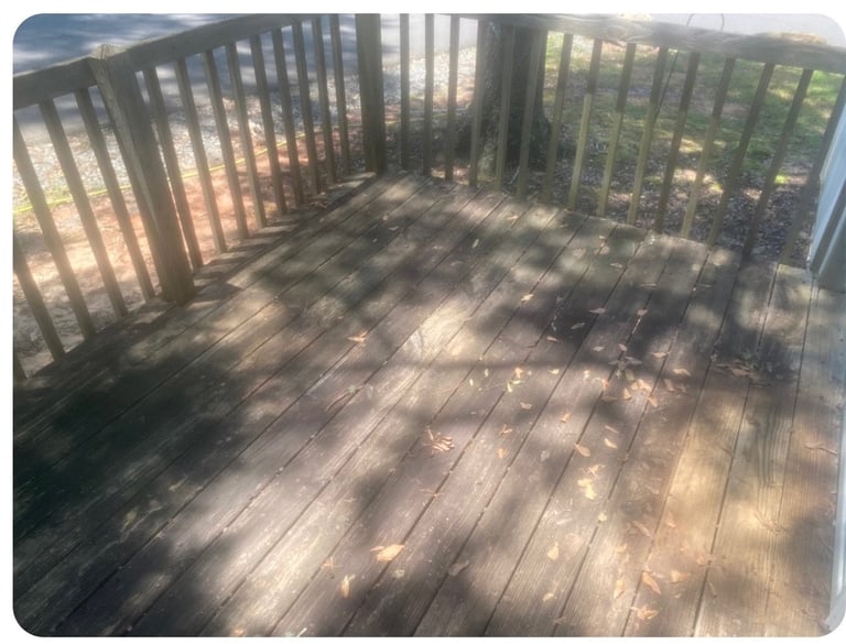 Wooden deck with dark railing overlooking green trees, dappled sunlight casting shadows on the deck boards