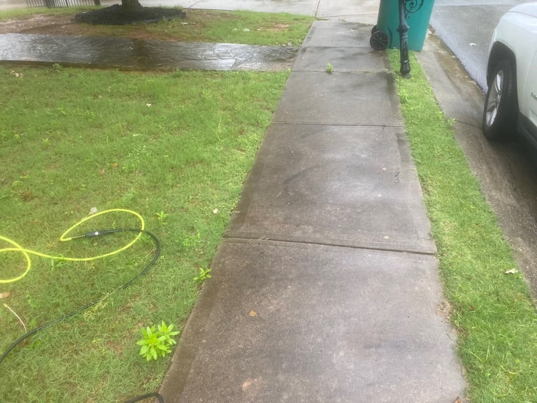 Long concrete sidewalk between grass and parked cars with a yellow garden hose on the lawn