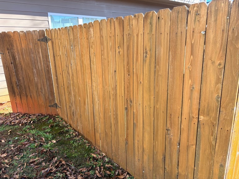 Wooden privacy fence with vertical slats in a residential backyard with mulch and grass below