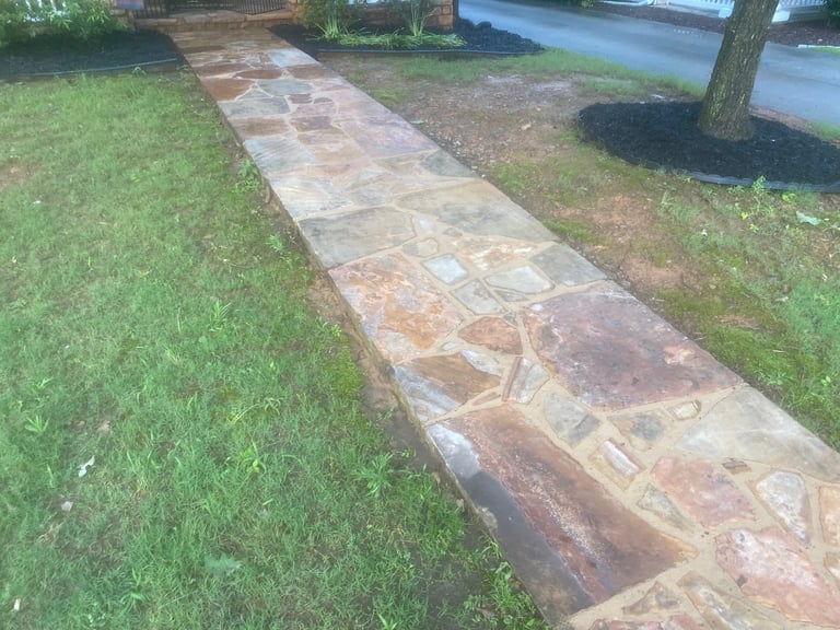 Stone pathway cutting through green grass with trees and water feature in background