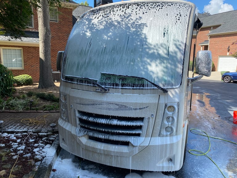 White RV motorhome being washed with soapy water in residential driveway
